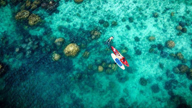 Top aerial view of Group of tourist are enjoy on water sport paddle sup-board with kayaking along at the edge of the sea beach under crystal clear of water in the island of summer trip