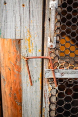 Rusty wire hook latch securing a mesh door on a weathered farm building © Vasilisa Dorofeeva