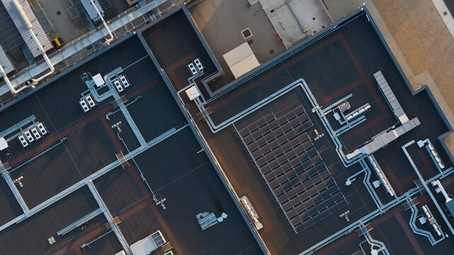 Aerial view of a flat industrial roof featuring multiple HVAC units and a solar panel array under warm sunlight in Bracknell, England, United Kingdom.
