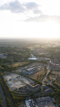 Aerial view of a commercial business park featuring modern office buildings, parking lots, and surrounding greenery near a railway line at sunset, Bracknell, England, United Kingdom.