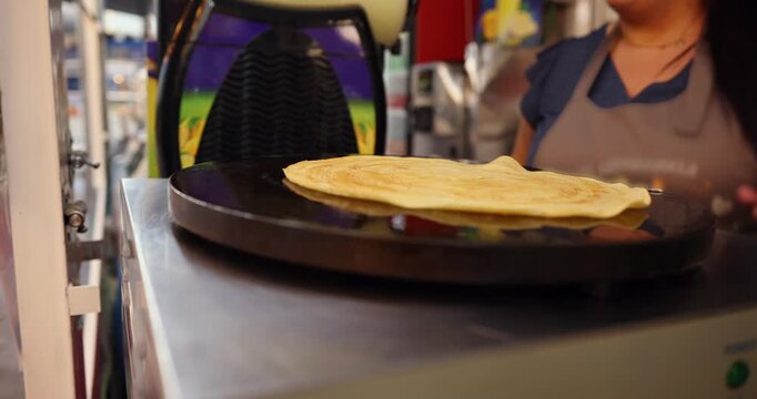 Skilled female vendor cooking a traditional french crepe on a hot plate, folding the delicious sweet pancake with a spatula to prepare it for serving at a local food market stall