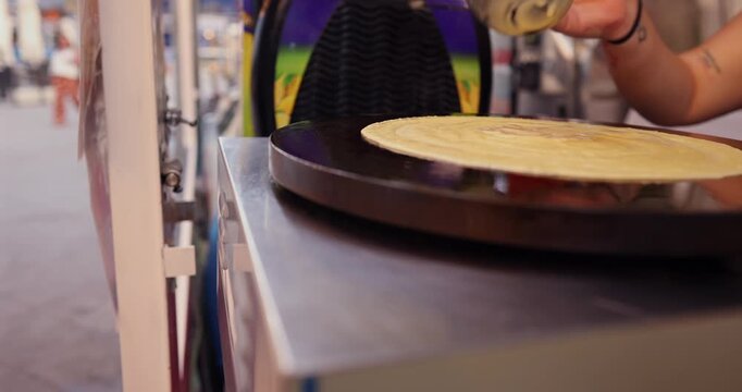 Close up of a street food vendor expertly preparing a traditional sweet crepe, spreading the batter and folding the thin pancake on a hot plate at an outdoor food stall during an evening fair