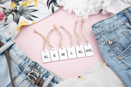 Various clothing sizes XS, S, M, L, XL on white wooden tags with clothes.