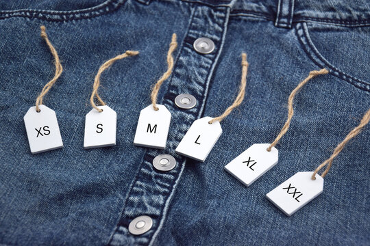 Various clothing sizes XS, S, M, L, XL on white wooden tags on the jeans background.