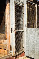 Homemade poultry coop entrance with weathered wooden door, wire mesh and rusty hook latch © Vasilisa Dorofeeva