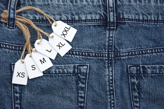 Various clothing sizes XS, S, M, L, XL on white wooden tags on the jeans background.