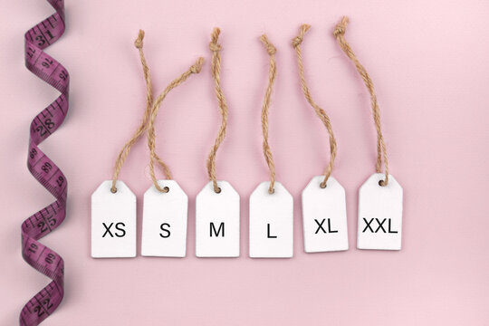 Various clothing sizes XS, S, M, L, XL on white wooden tags on the pink background.