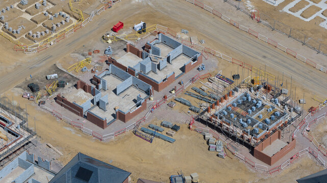 Aerial view of a residential construction site featuring brick foundations and concrete block walls under clear daylight in Basingstoke and Deane District, England, United Kingdom.
