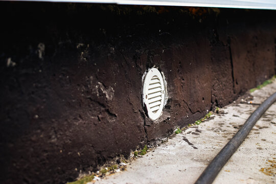 Round plastic foundation vent grille set into a weathered concrete base