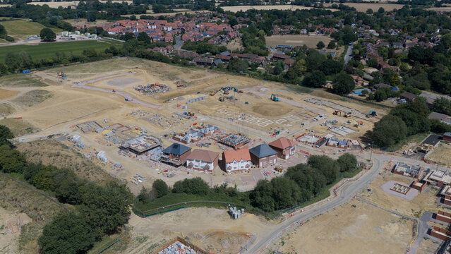 Aerial view of a residential construction site featuring partially built houses, heavy machinery, and excavated land in Basingstoke and Deane District, England, United Kingdom.
