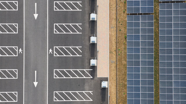 Aerial view of a parking lot with marked pedestrian crossings and white directional arrows adjacent to a large array of solar panels in Winchester, England, United Kingdom.