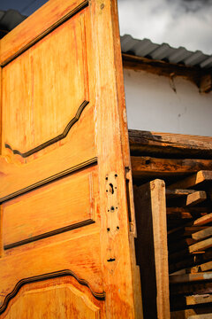 Paneled wooden door leaning against a stack of weathered boards in a rustic farmyard