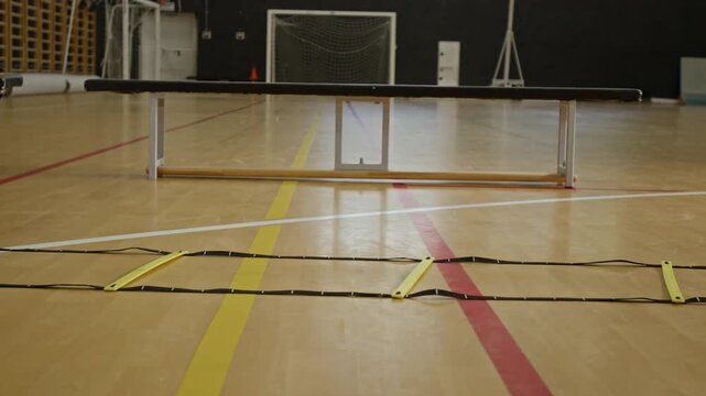 Unrecognizable children training on agility ladder in indoor sports hall, focusing on footwork and coordination. Footage is ideal for youth sports promotions and athletic footwear commercials