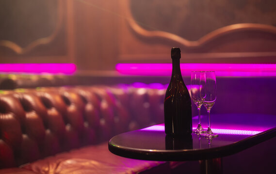 Champagne bottle and glasses in neon vip lounge.