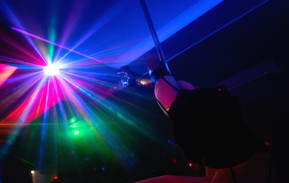 Pole dancer performing under laser lights in club.