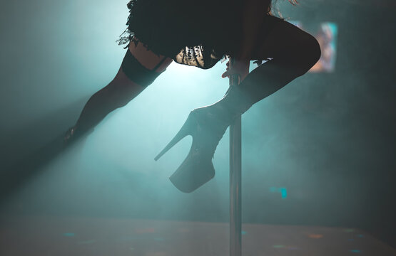 Pole dancer performing trick in smoky club.