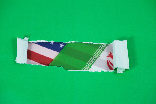 Iranian and US flags behind torn green paper. US-Iran conflict.
