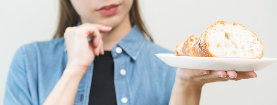 Gluten allergy, asian young woman hand holding, refusing to eat white loaf on plate in breakfast food meal, girl stand thinking isolated on background. Gluten intolerant and Gluten free diet concept.