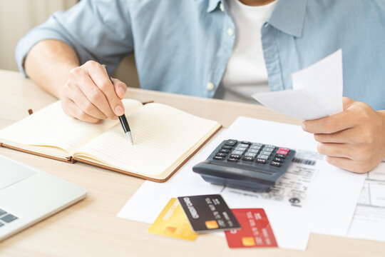 Stressed asian young businessman hand write management budget for saving cost expenses of monthly, male holding bills and receipt for to payment on table at home. Financial, finance of banking concept