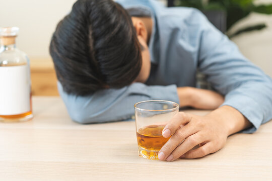Health care alcoholism drunk, fatigue asian young man hand holding glass of whiskey, alone depressed male drink booze on sofa at home. Treatment of alcohol addiction, suffer abuse problem alcoholism.