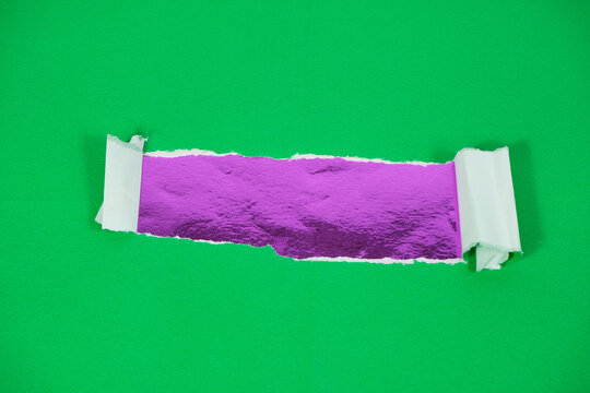A purple foil layer beneath torn green paper. Torn paper revealing a purple-backed area for text. The torn green paper layer is pulled back, exposing the purple foil layer underneath.
