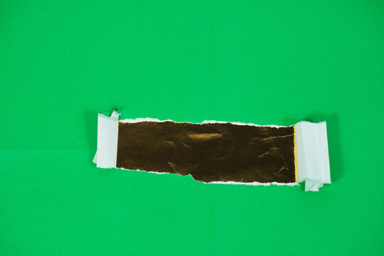 A gold foil layer behind torn green paper. Torn paper revealing a gold-backed area for text. The torn green paper layer peels back, exposing the gold foil layer underneath.
