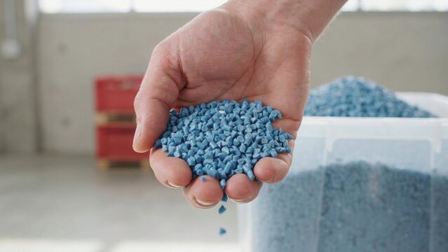 Hand holding blue plastic polymer pellets for industrial manufacturing and resin production