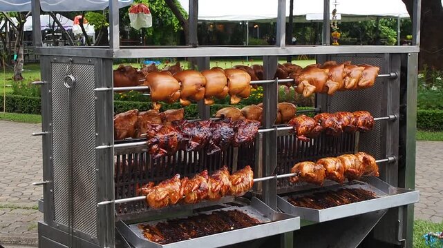 Whole rotisserie chickens roasting on large outdoor spit grill