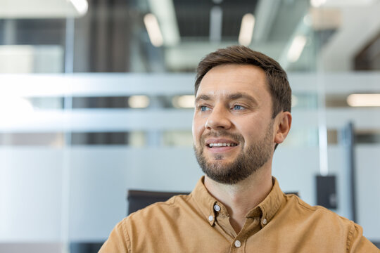 Confident young businessman in a modern office environment looking away with a smile, representing success, future vision, and professional growth in his career