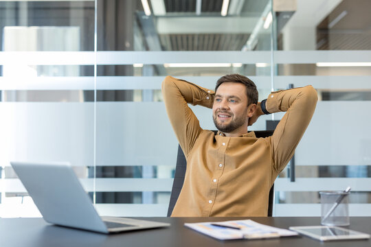Young businessman relaxing with hands behind head, enjoying a moment of satisfaction and success in a modern office environment after completing his tasks