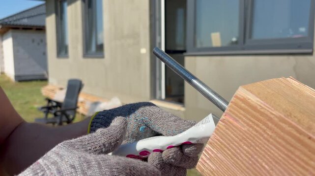 A builder applies glue to a threaded rod in a wooden beam.