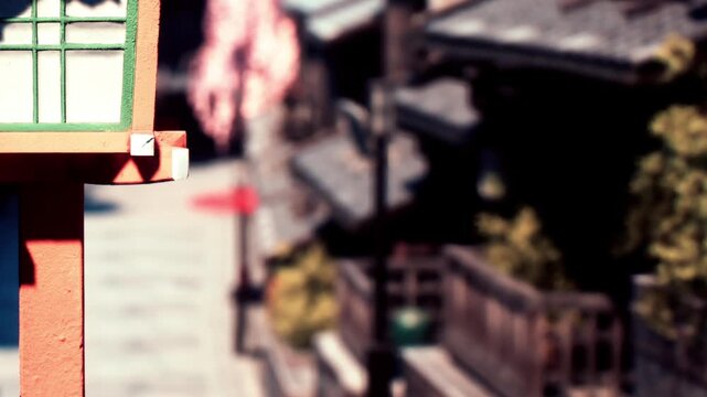 A red and green lantern stands in focus next to traditional buildings in a narrow street. It is daytime and the buildings show the rustic style of the area.