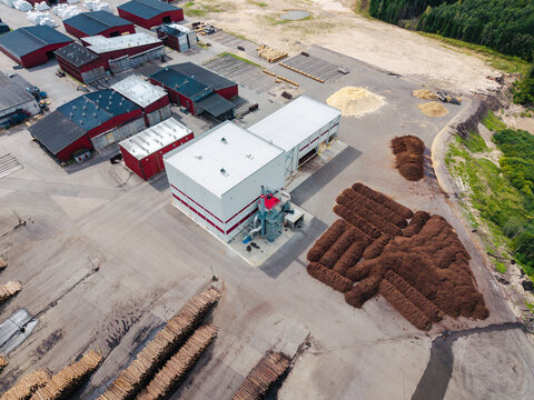Aerial view of a large sawmill facility featuring industrial buildings, stacks of sawn timber, and piles of wood chips in Lauciene Parish, Talsi Municipality, Latvia.