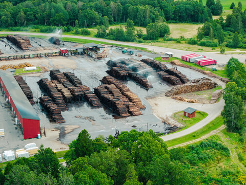 Aerial view of a timber processing facility with stacks of logs being sprayed with water, surrounded by forests and rural landscape in Lauciene Parish, Talsi Municipality, Latvia.