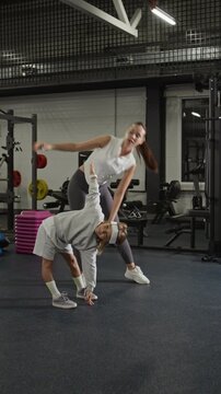 Vertical video of Caucasian female trainer helping Caucasian child perform side bend stretch in gym. Clip is ideal for family fitness, youth sports, and healthy lifestyle marketing campaigns