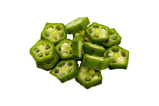 A pile of freshly sliced okra pieces, showing green pentagonal skins and white seeded interiors on a light yellow background