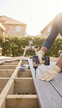 Builder securing decking board with power drill outdoors