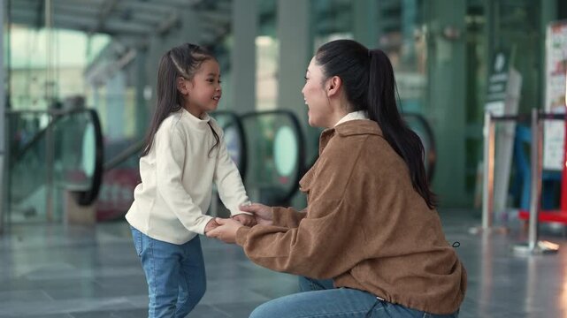cheerful mother holding hand her daughter while talking and laughing on the city street