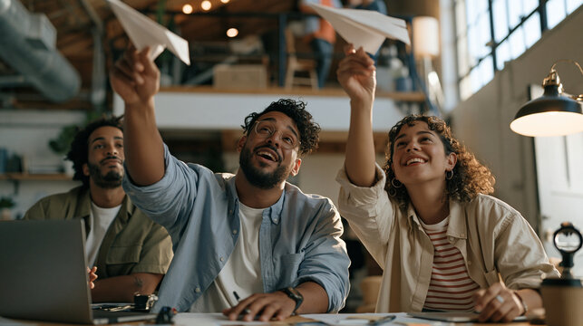 A diverse film editing team sprawls across a quiet rural barn conversion studio, launching paper airplanes from laptop stands toward an open loft door, startup dream and ambition
