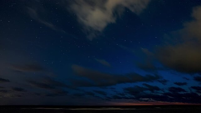 Starry night sky timelapse with drifting clouds over a dark horizon line during twilight in a smooth, cinematic nature timelapse. Perseid meteor shower visible over the Europe.