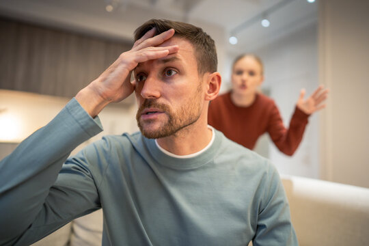 Frustrated man tired with woman partner conflict escalation, married couple in disagreement crisis, family communication troubles, manipulative husband sitting on couch distancing from mad wife.