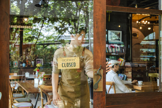 Young barista cafe owner flipping sign to open on storefront door, welcoming customers with confident smile, small business startup energy and positive service mindset in hospitality environment.