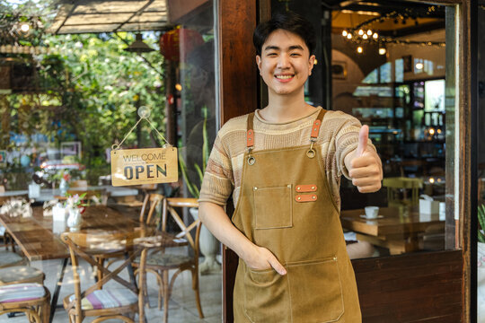 Small business cafe owner barista opening door while holding smartphone welcoming customer into coffee shop showing service interaction and daily business routine, young generation startup business