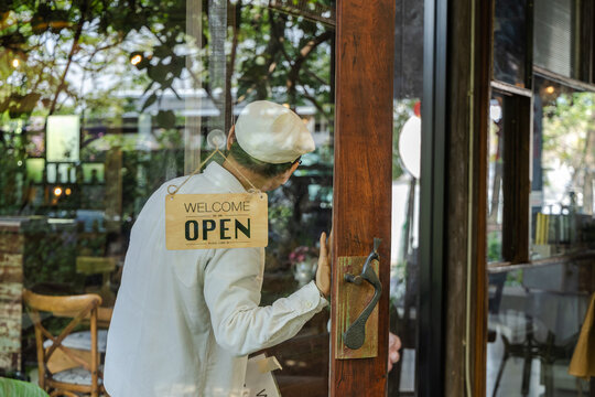 Family small business, senior cafe owner placing hiring sign on glass door, recruitment and expanding team concept in local coffee shop and restaurant. Cafe owner teaching barista about work process