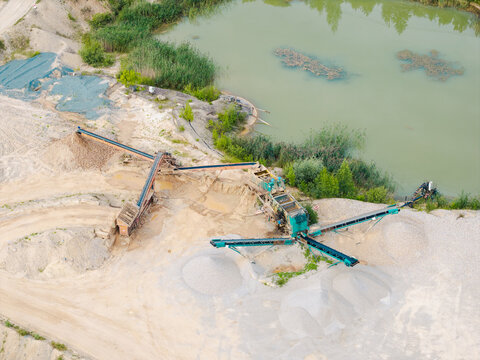 Aerial view of a gravel pit with industrial machinery and conveyor belts situated next to a pond in Slampe parish, Tukums Municipality, Latvia.