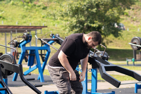 overweight middle aged man bends forward with fatigue at an outdoor gym, illustrating beginner exercise, physical effort, health motivation, realistic fitness and recovery