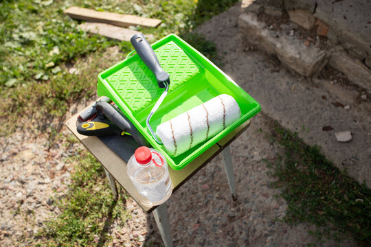 paint roller, tray and restoration tools prepared outdoors beside a house, showing equipment for repainting a metal entrance door during practical diy renovation