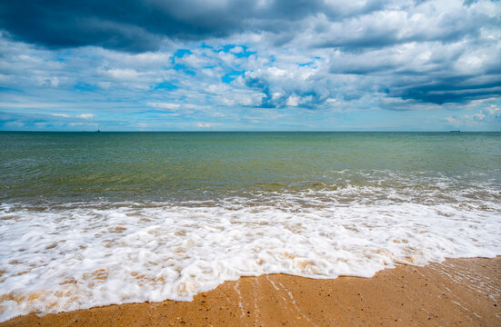 Foaming North Sea waves reaching the sandy shore beneath a dramatic cloudscape at Waxham Beach near Horsey Gap on the Norfolk coast of England.