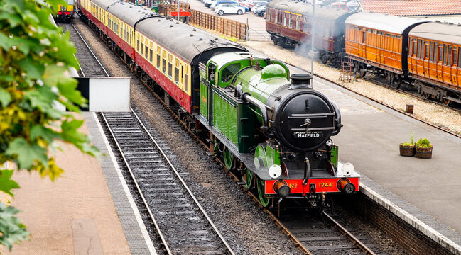 Historic green steam locomotive with carriages at a station on a preserved heritage railway line in Norfolk, England. Elevated view of platform, tracks and rolling stock.