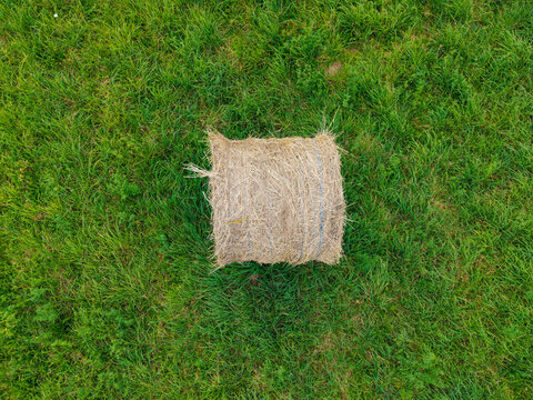 Aerial view of a single round hay bale resting in a lush green field in Latvia.